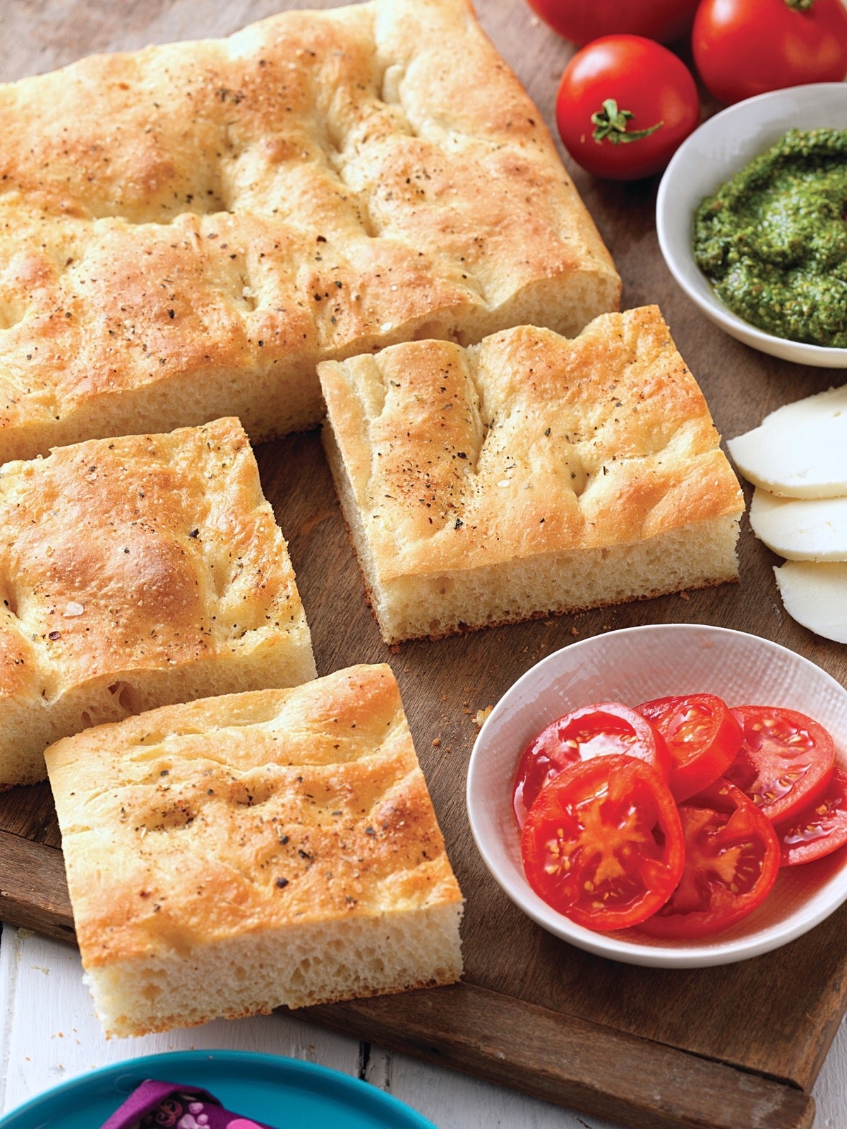 No-Fuss Focaccia cut into squares on a serving board with tomato, pesto, and mozzarella on the side.