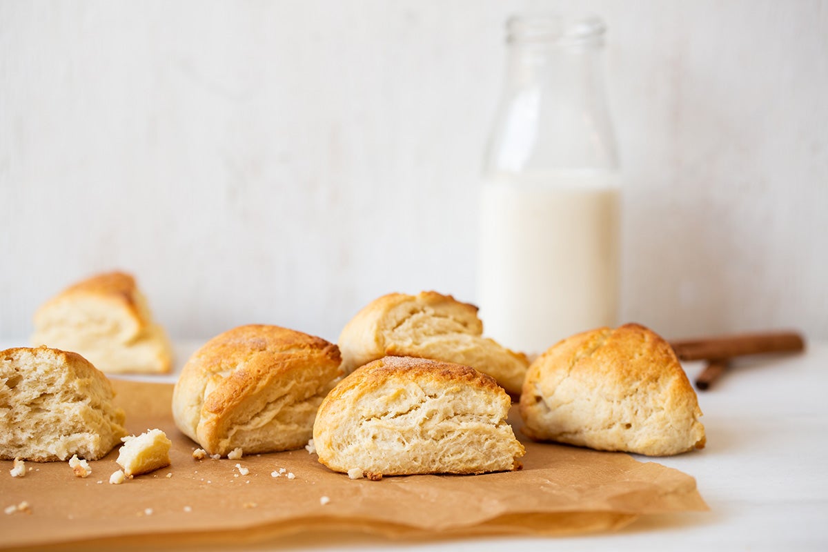 A pile of Cream Tea Scones on a kitchen table with a glass bottle of cream in the background