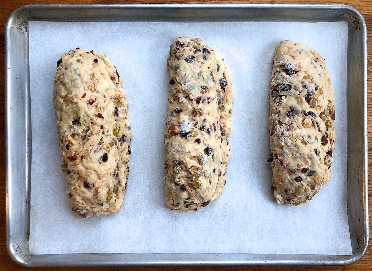Three stollen positioned on a parchment lined baking sheet, ready to rise.