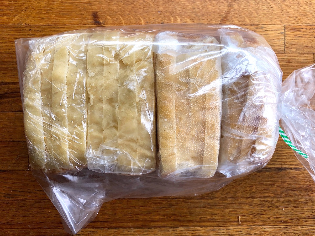 Individual packets of white sandwich bread slices wrapped in plastic and stacked in a large plastic bread bag for freezer storage.