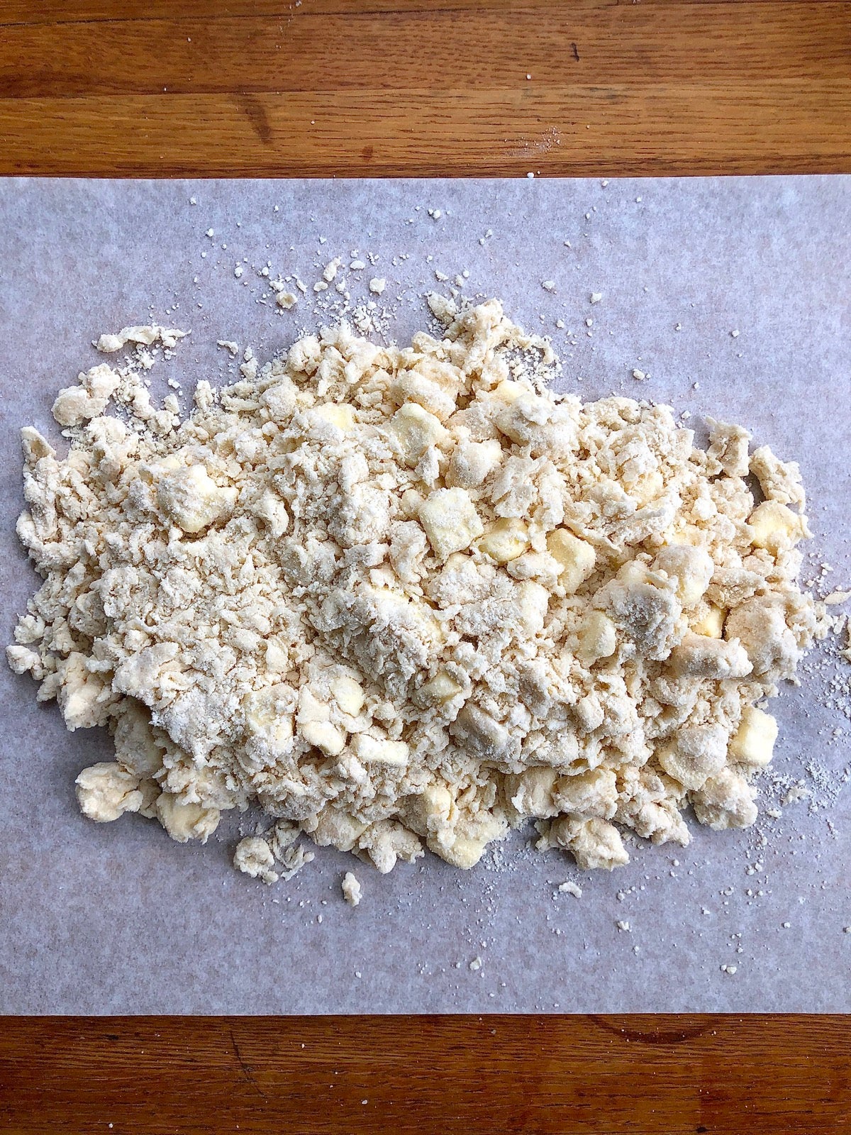 Dry clumps of pie crust dough on a sheet of parchment.