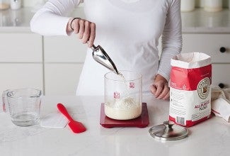Measuring flour into a bowl set on a digital scale.