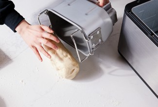 Baker removing proofed bread dough from bread machine bucket