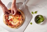 Neapolitan pizza being garnished with basil