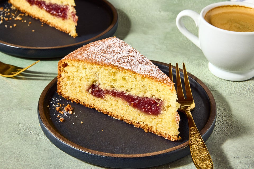 A slice of Jelly Doughnut Cake on a dark plate with a golden cake, jelly filling, and lovely brown exterior.