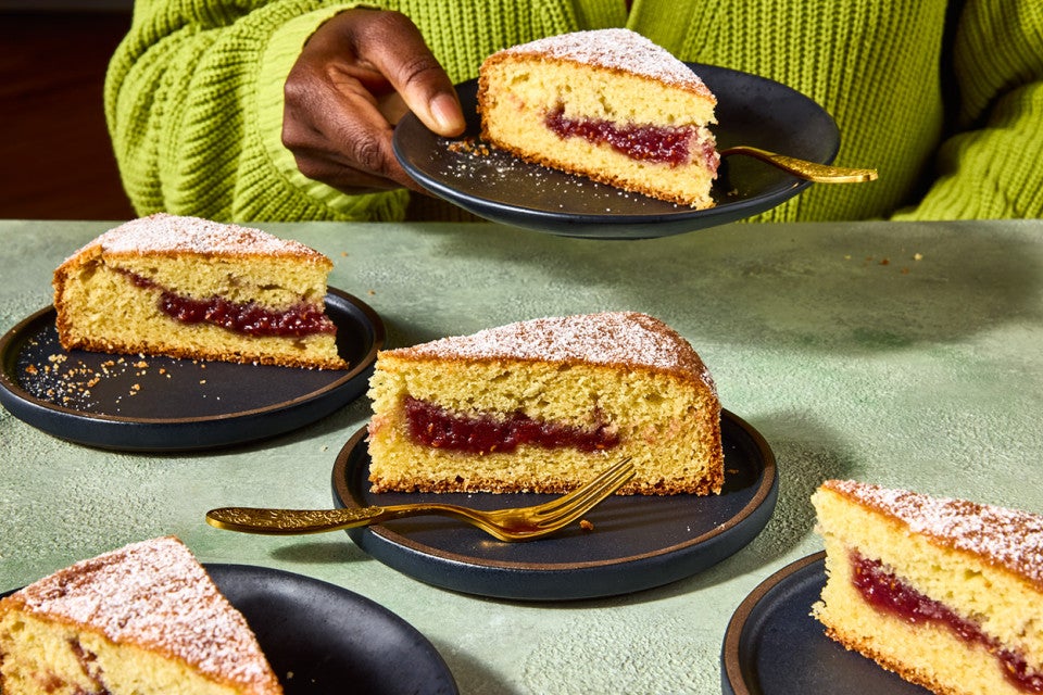Multiple slices of Jelly Doughnut Cake arranged on a counter with a person in the background holding a plated slice.