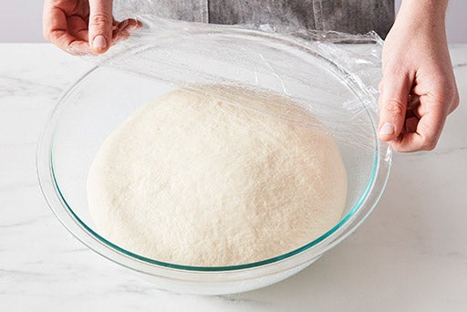 A glass bowl of risen dough that is quite puffy. 