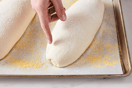 A baker poking a loaf of bread to see if the dough is fully risen, the dough bounces back after being touched. 