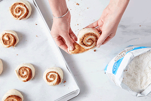 A baker tucking the ends of the dough underneath each roll to prevent them from uncoiling while baking.