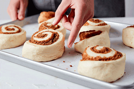 A baker gently pressing on a roll to see if it's fully proofed. 