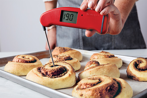 A baker using a Thermapen to check the internal temperature of a baked cinnamon roll.