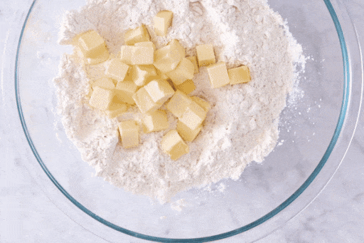 Chunks of butter being tossed in the flour mixture and a baker using their fingers to flatten the chunks of butter. 