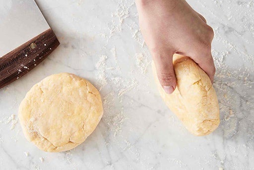 A baker rolling the disc of dough on the countertop to smooth the edges. 