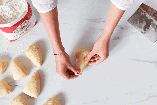 A baker shaping dough into rolls by folding the corners into the center and then rounding the dough into a ball.