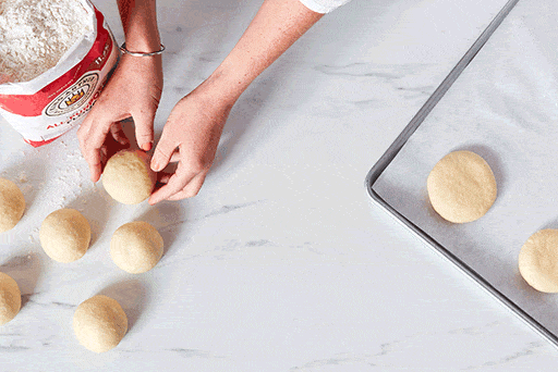 A baker using the palm of their hand to gently flatten each roll. 