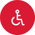 A white icon of a person in a wheelchair over a red circular background.