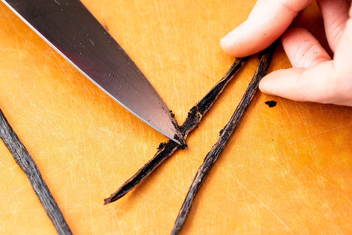 A baker's hand using a knife to scrape out the vanilla seeds from the bean.