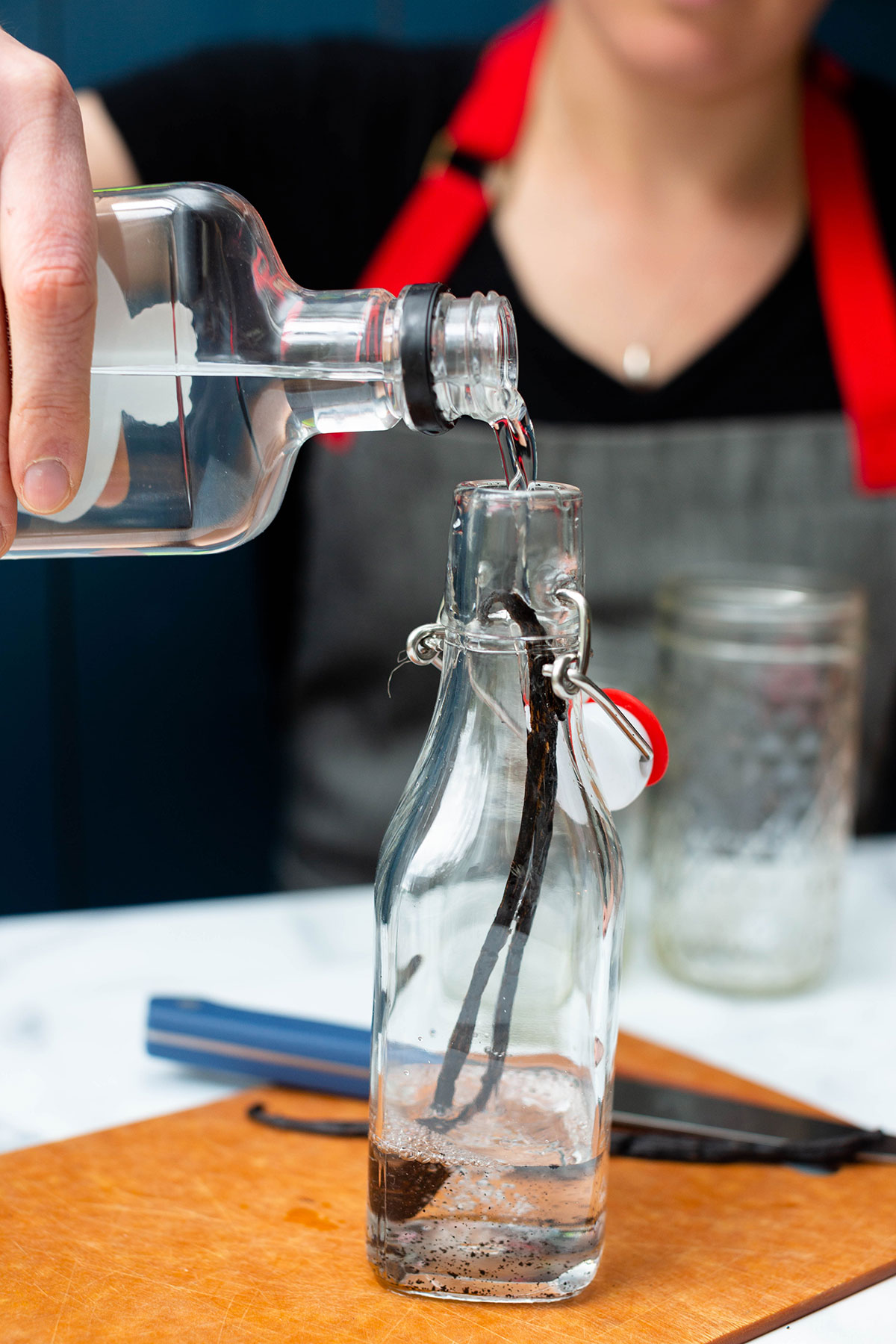 A baker pouring vodka into a bottle with a vanilla bean to start the process of making homemade vanilla extract.