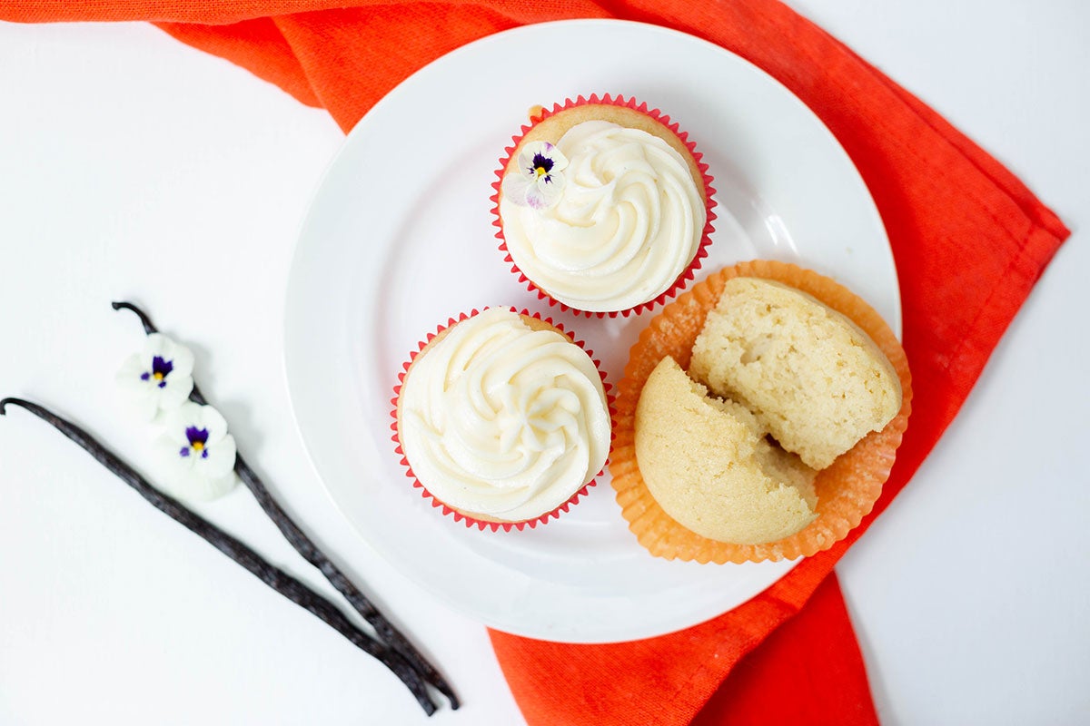 Vanilla bean cupcakes topped with frosting and edible flowers along with two whole vanilla beans.