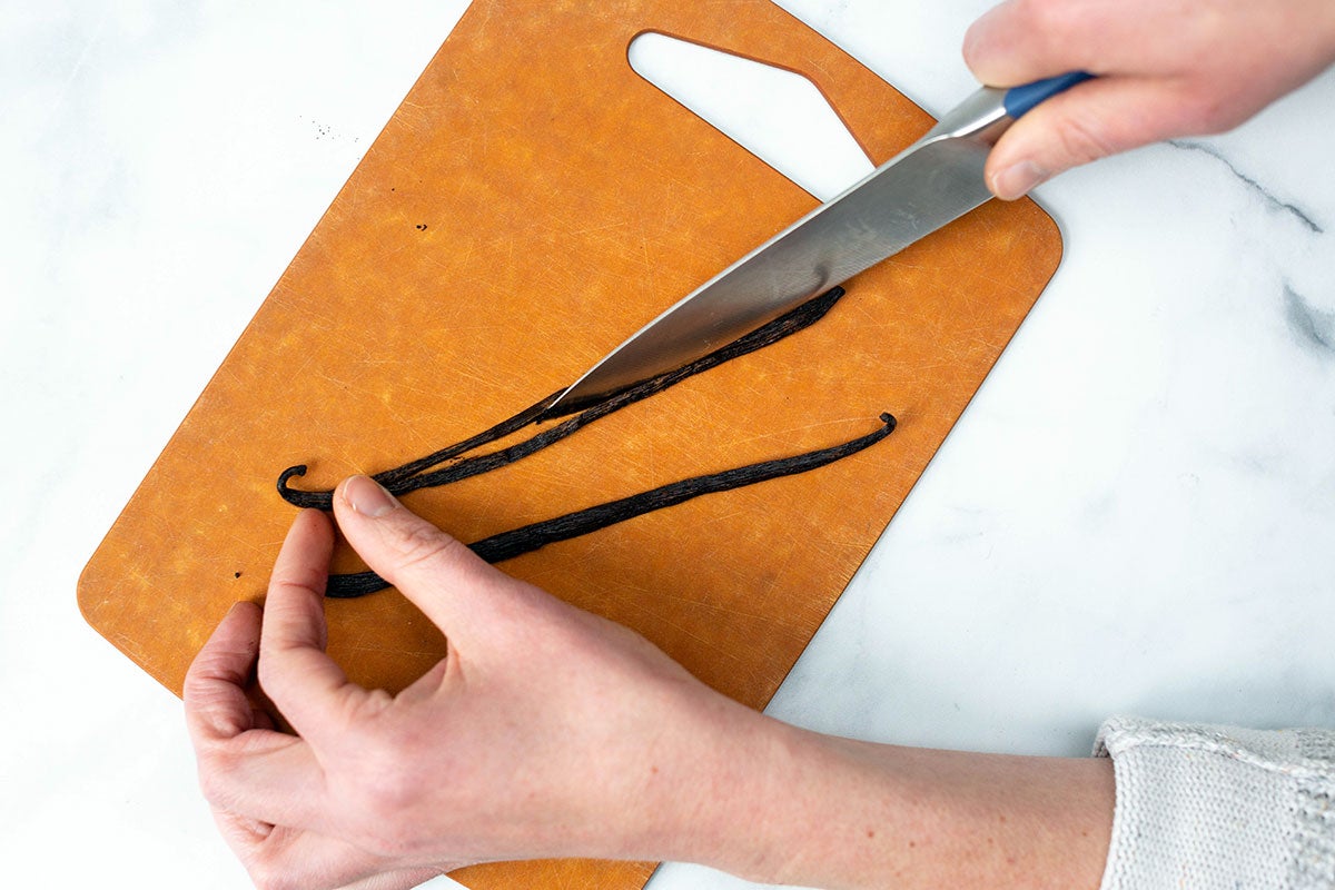 A baker splitting a vanilla bean lengthwise to prep it for homemade vanilla extract.