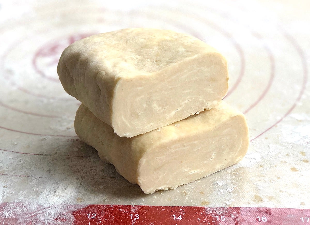 Log of pie crust dough cut in half, ready to roll