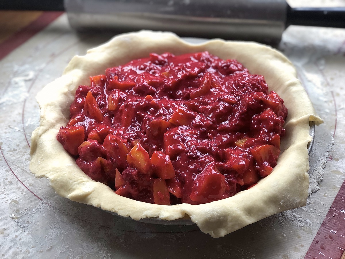 Pie crust in pan filled with peach-apricot-raspberry filling
