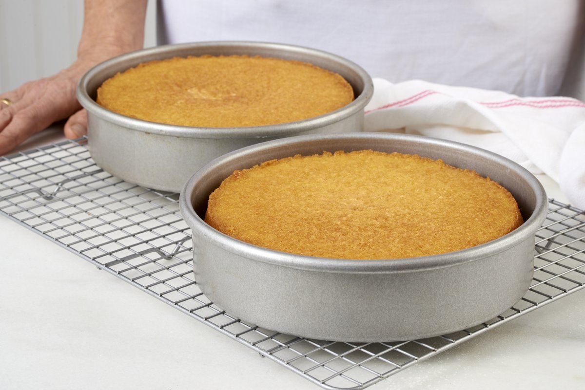 Two round cake pans of vanilla layer cake on a cooling rack that are golden brown