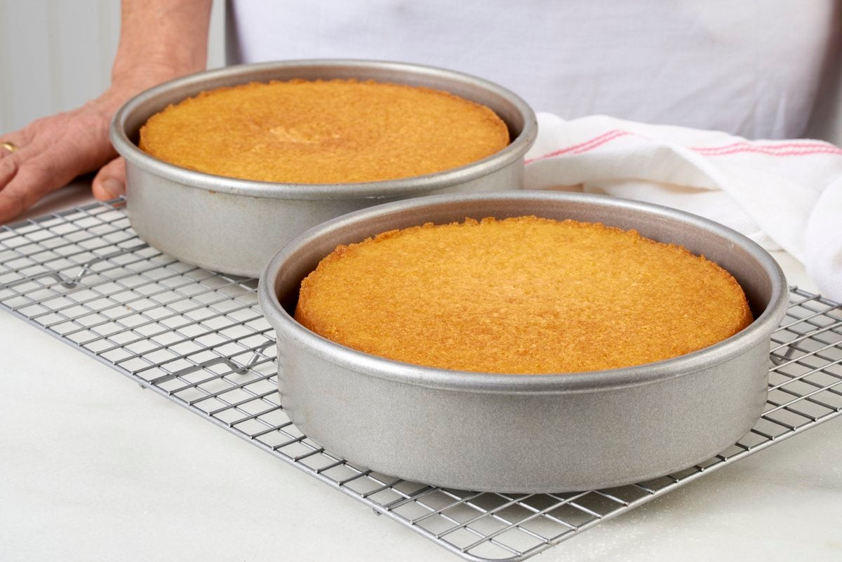 Two round cake pans of vanilla layer cake on a cooling rack that are golden brown