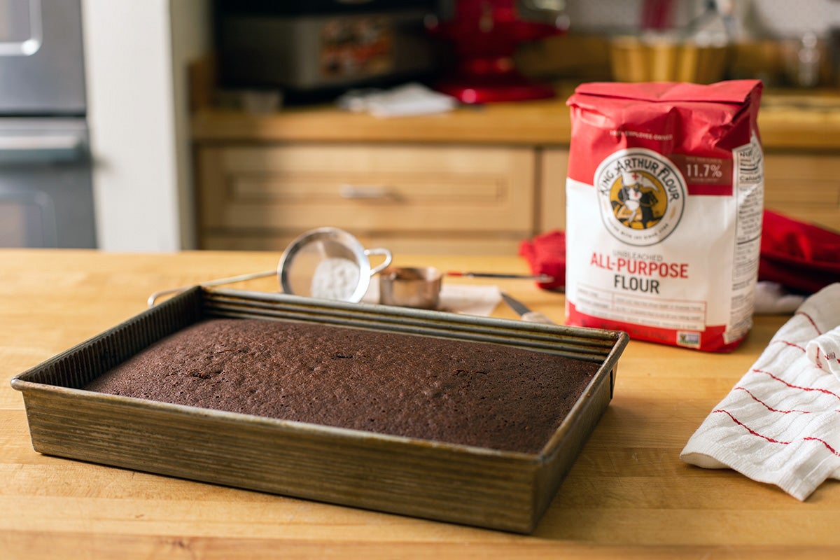 Chocolate sheet cake with a bag of King Arthur Flour, confectioner's sugar and cocoa powder on a wooden table