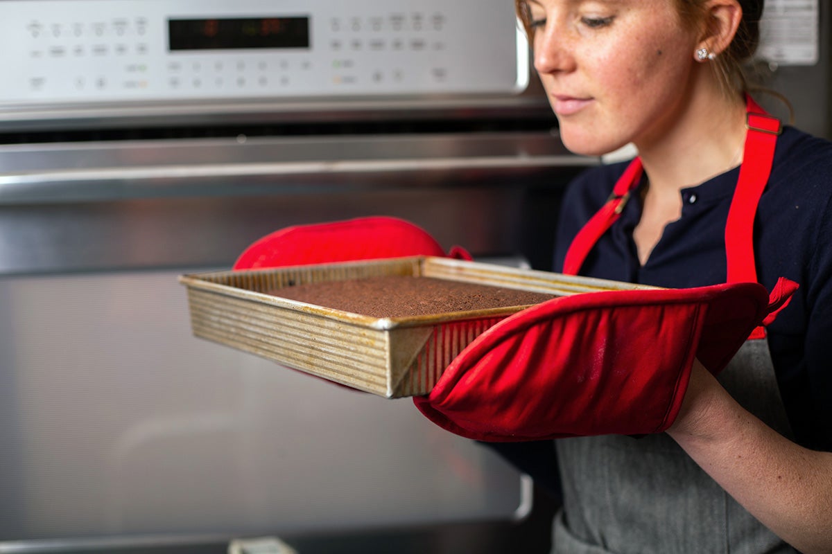 A baker taking in the smell of freshly baked chocolate cake in front of an oven