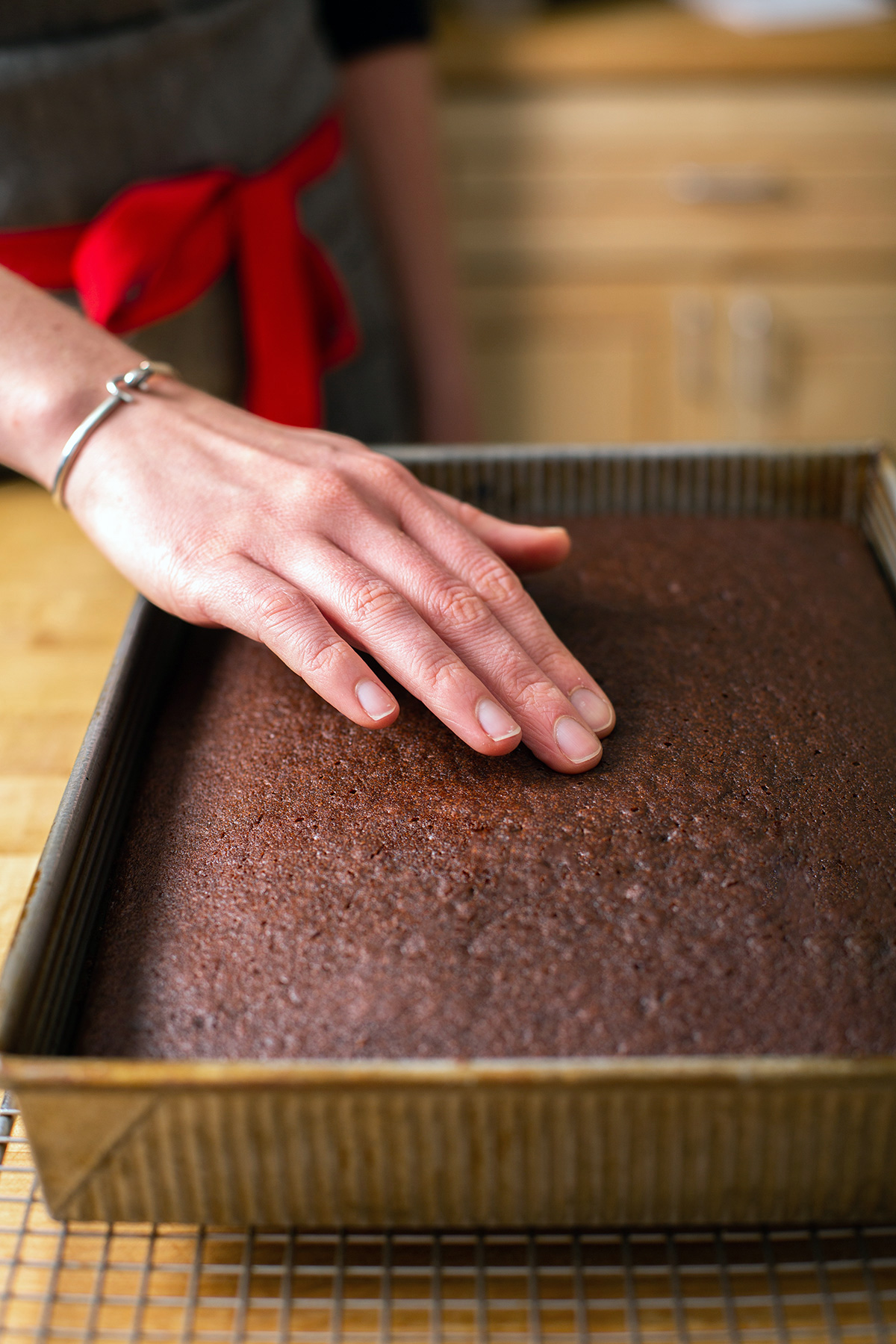 A baker pressing on the center of a chocolate cake to see if it's springy and done baking