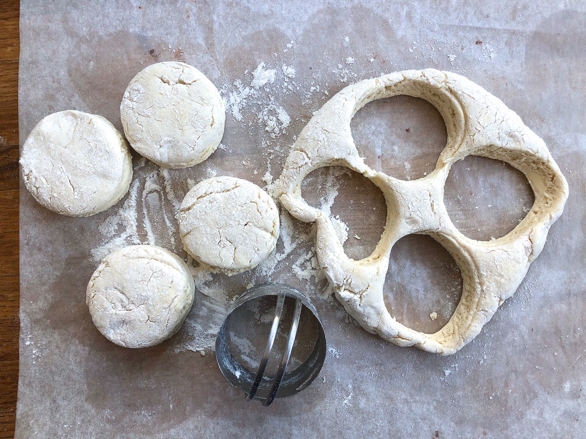 Four 2 3/8" biscuits cut from biscuit dough, scraps ready to be gathered and cut for more biscuits.
