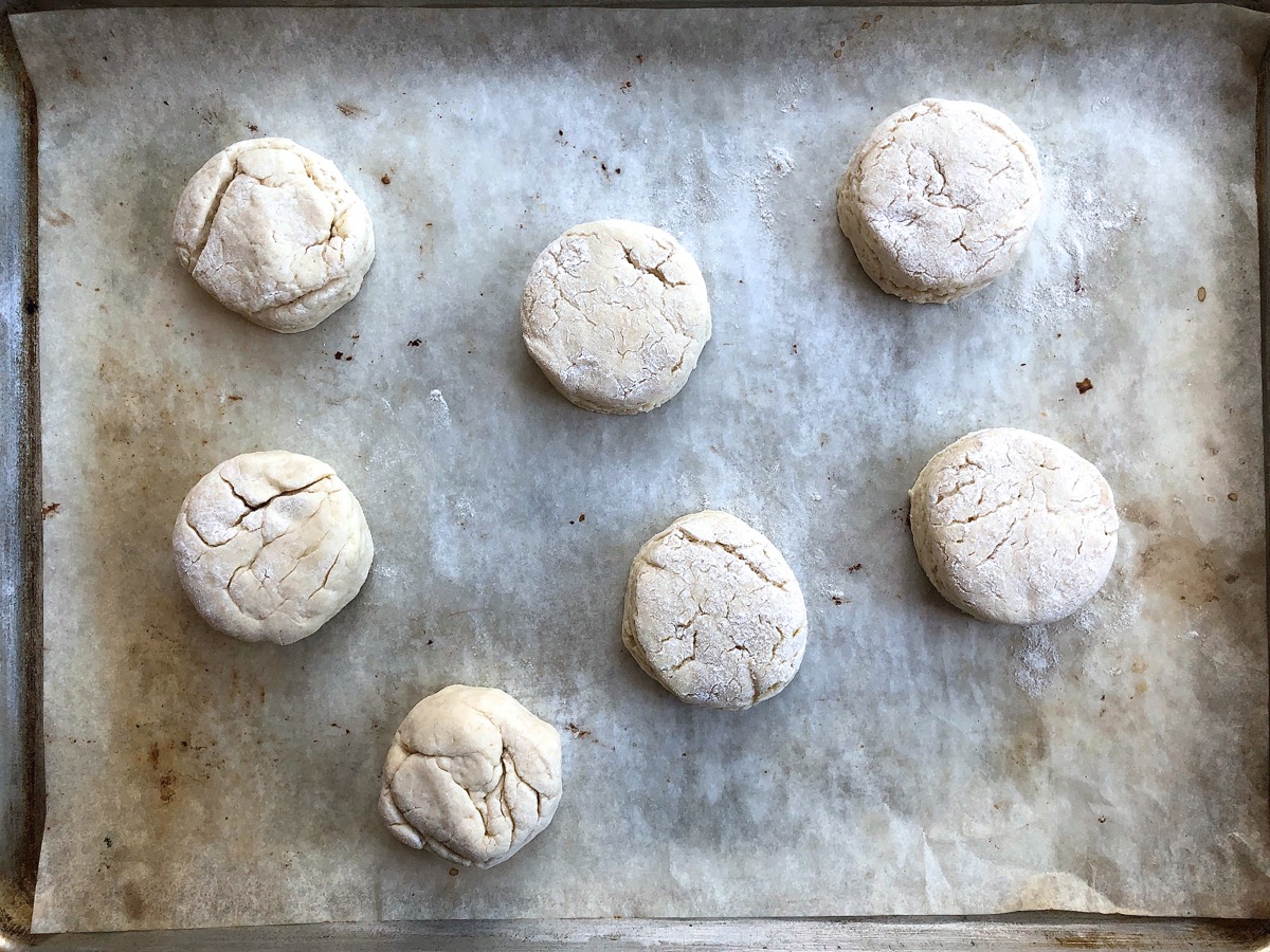 Seven biscuits spaced on a parchment-lined baking sheet, ready for the oven.