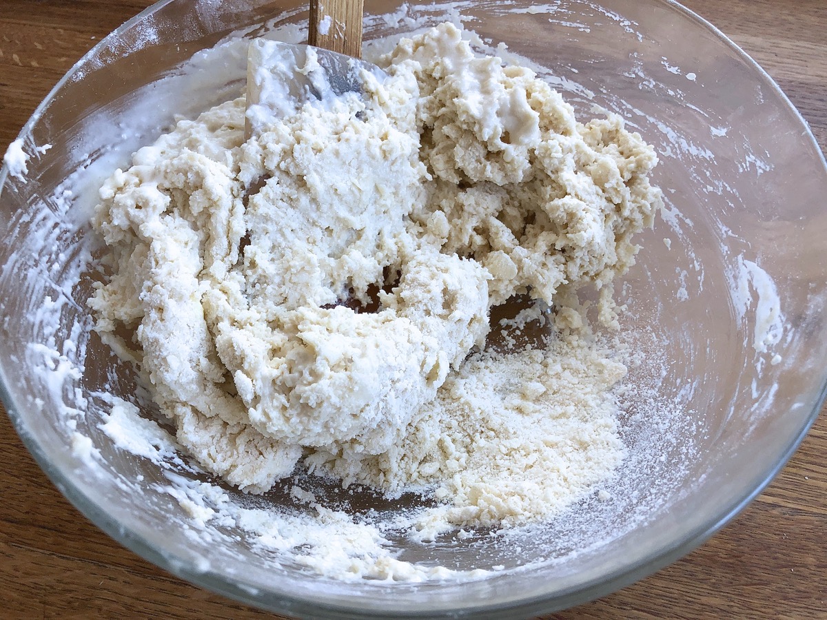 Cohesive biscuit dough in a bowl with some unincorporated floury crumbs underneath.