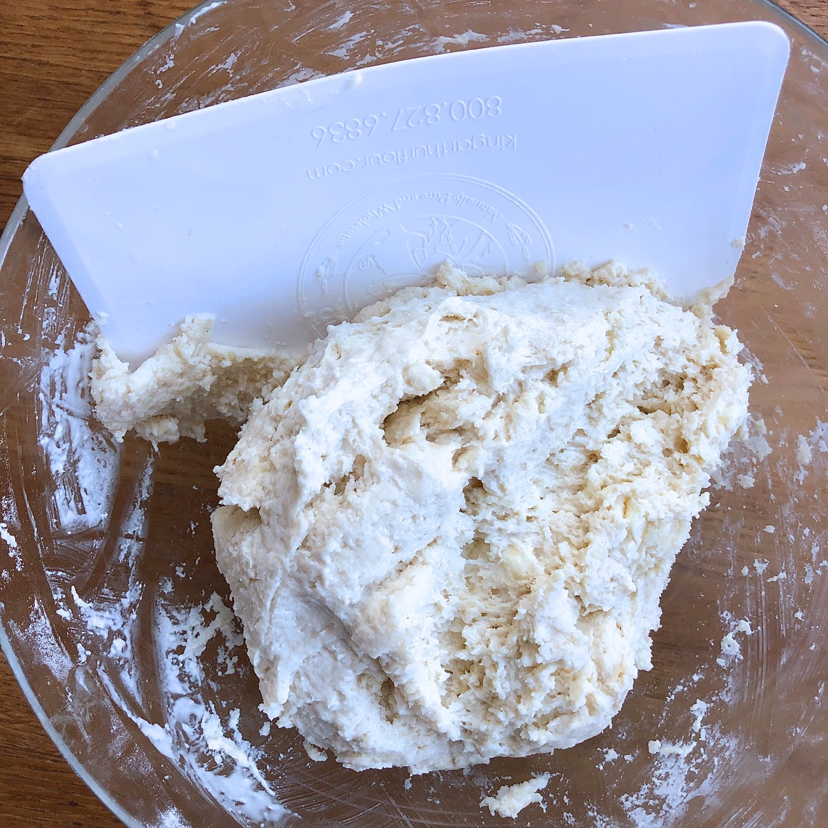 Using a bowl scraper to bring biscuit dough together in a bowl.