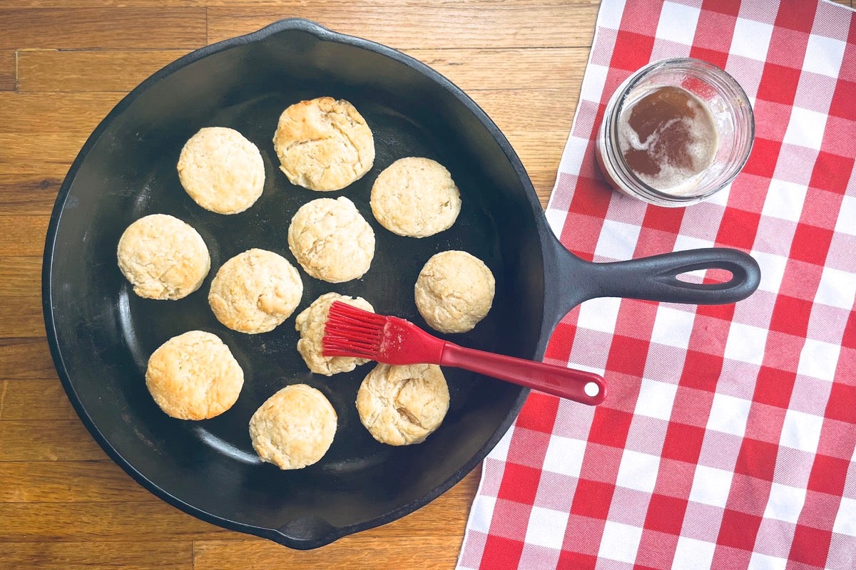 Sourdough biscuits in a cast iron frying pan being brushed with brown butter.