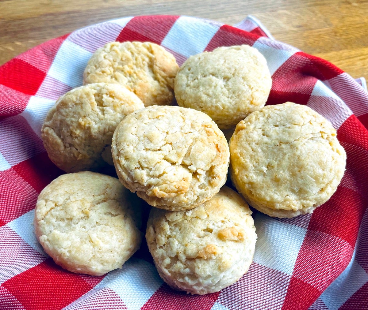 Sourdough biscuits in a woven basket lined with a red and white gingham towel.