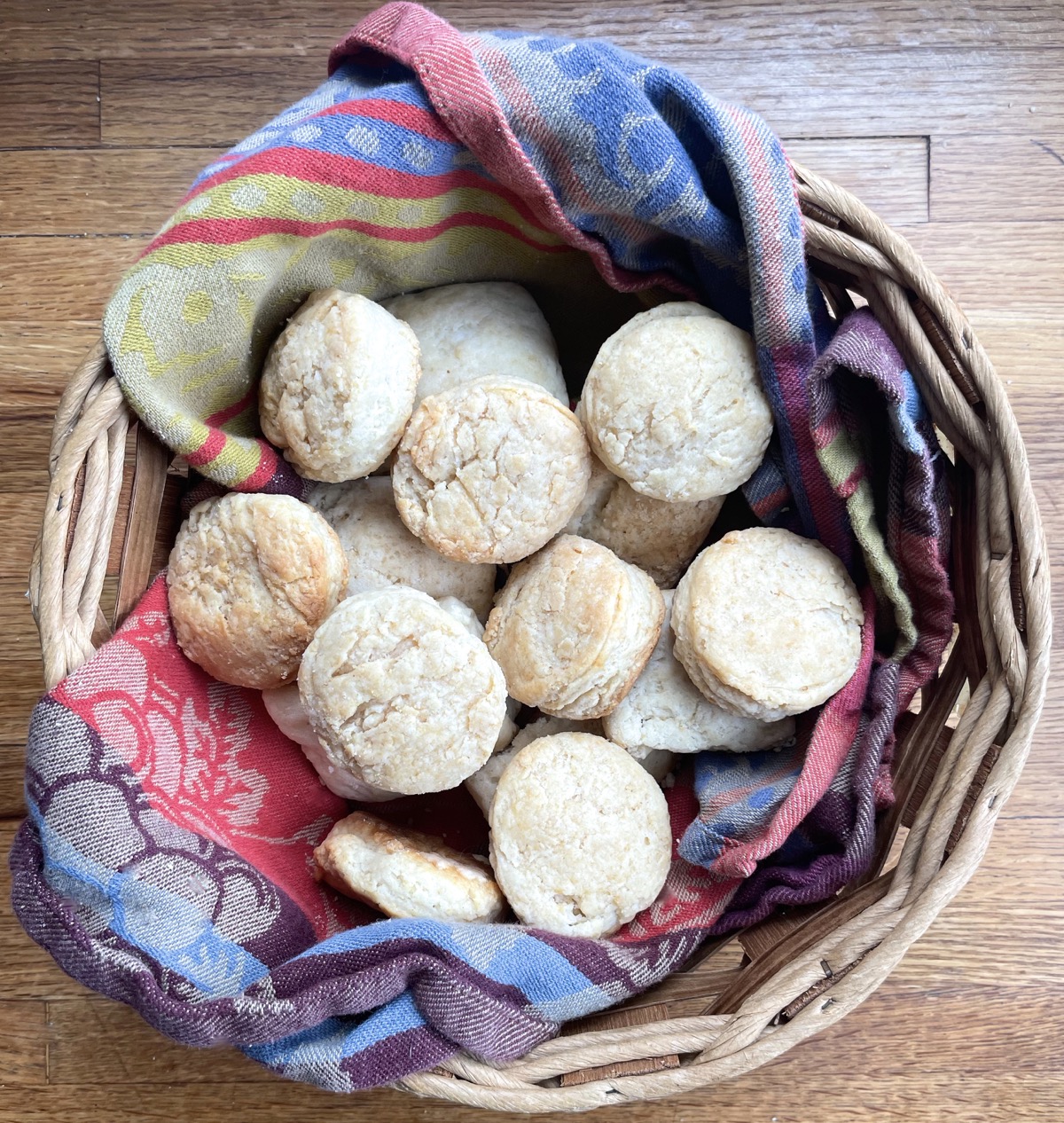 Baked sourdough biscuits in a woven basket lined with a colorful towel.