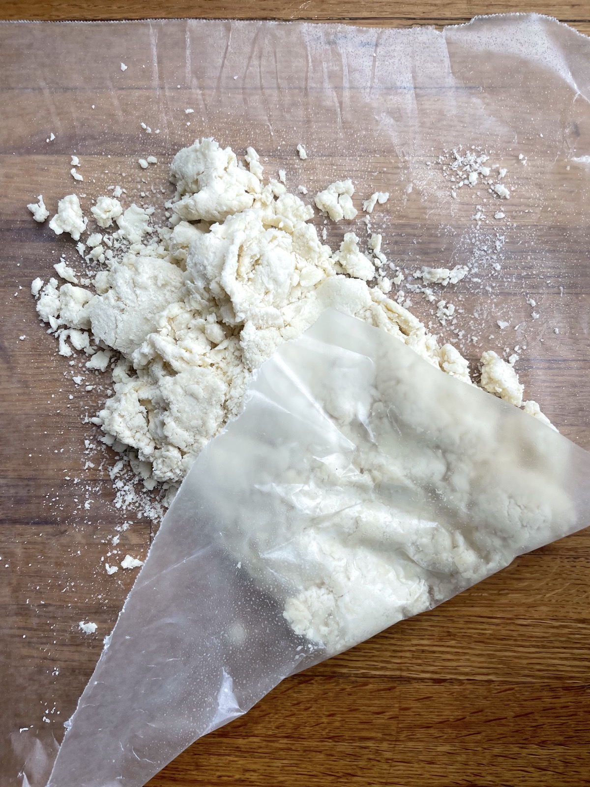 Crumbly biscuit dough on a piece of waxed paper, ready to be folded and patted into a rectangle. 
