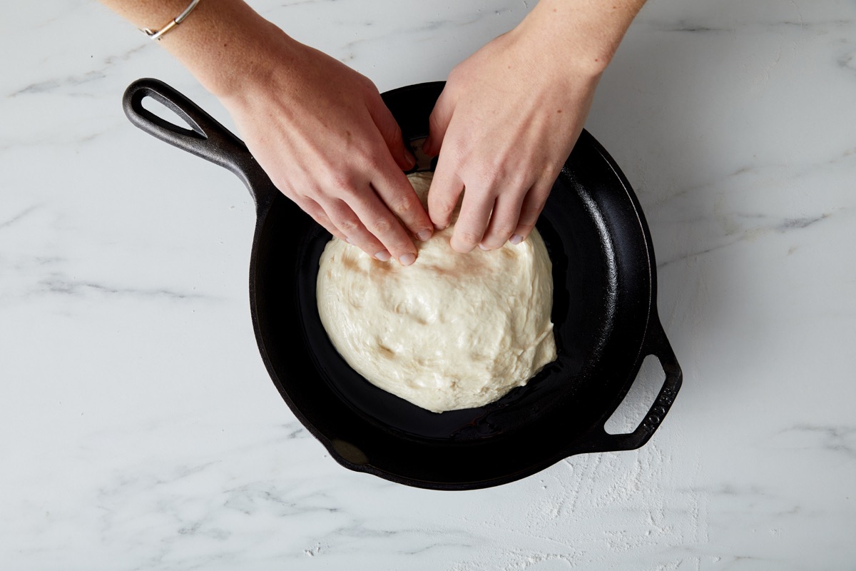 Pizza dough being spread into a cast iron skillet.