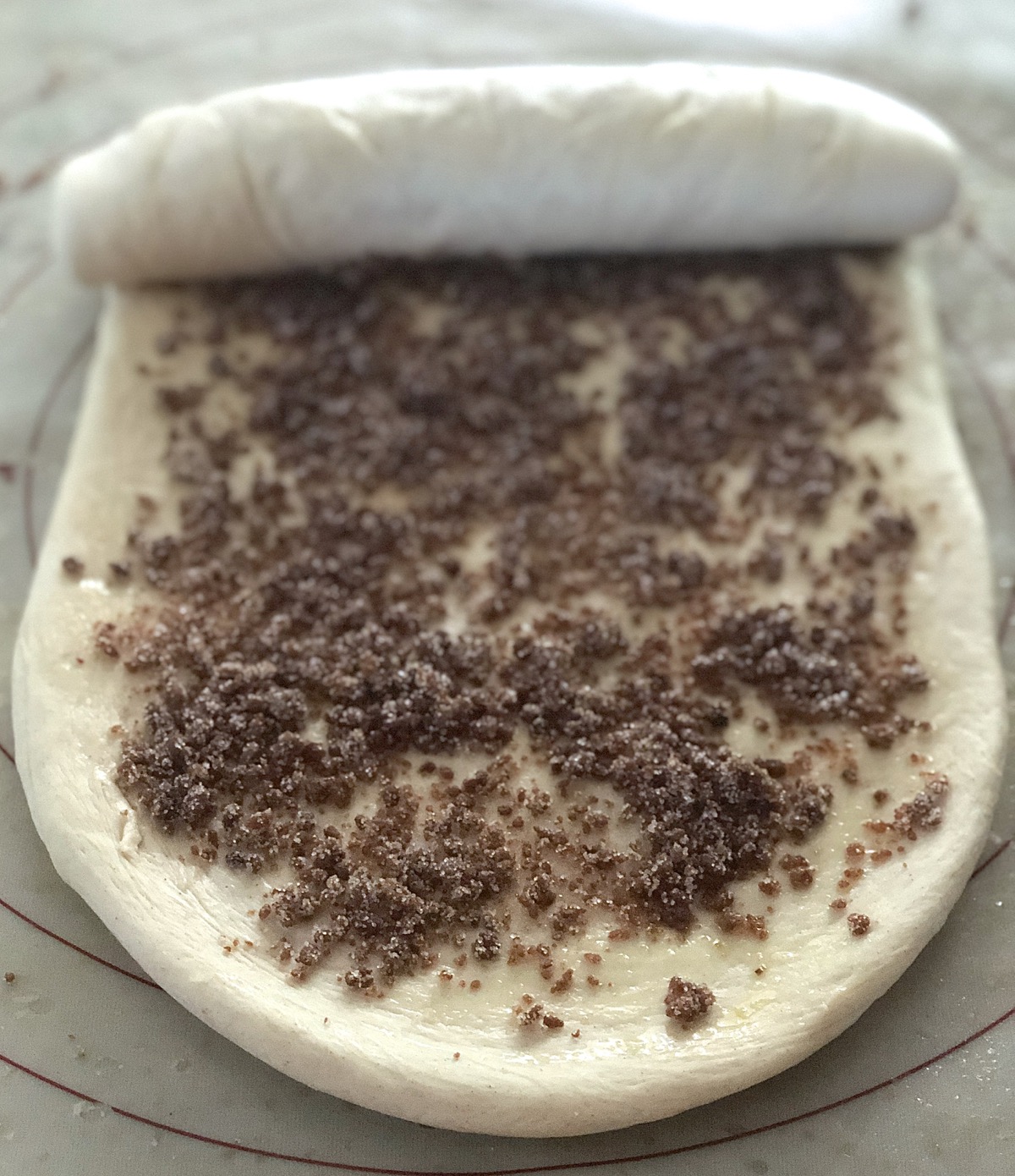 The dough for a cinnamon swirl loaf, sprinkled with filling and being rolled into a log.