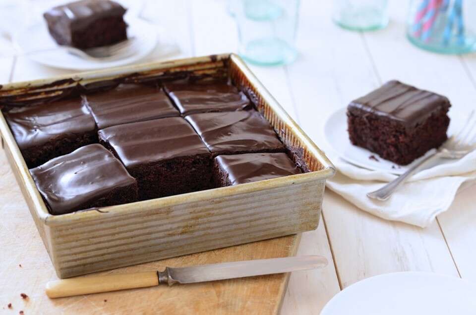 Chocolate cake with fudge frosting baked in a square pan, one piece taken out and set on a plate.