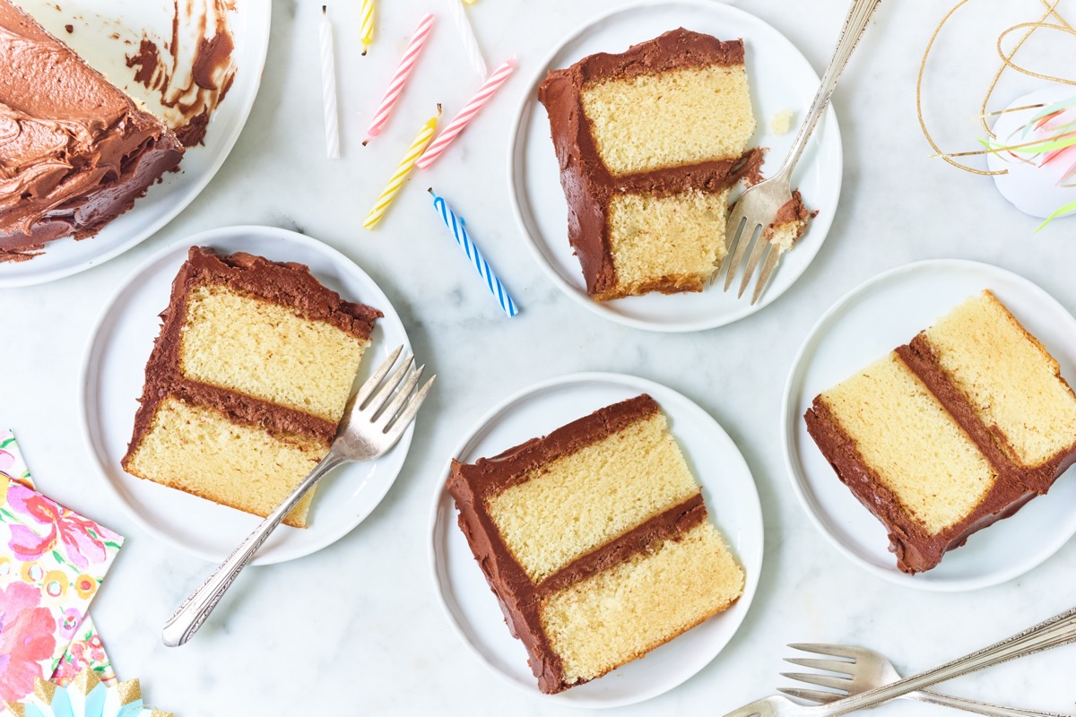 Slices of yellow layer cake with fudge frosting on a countertop, with birthday candles.