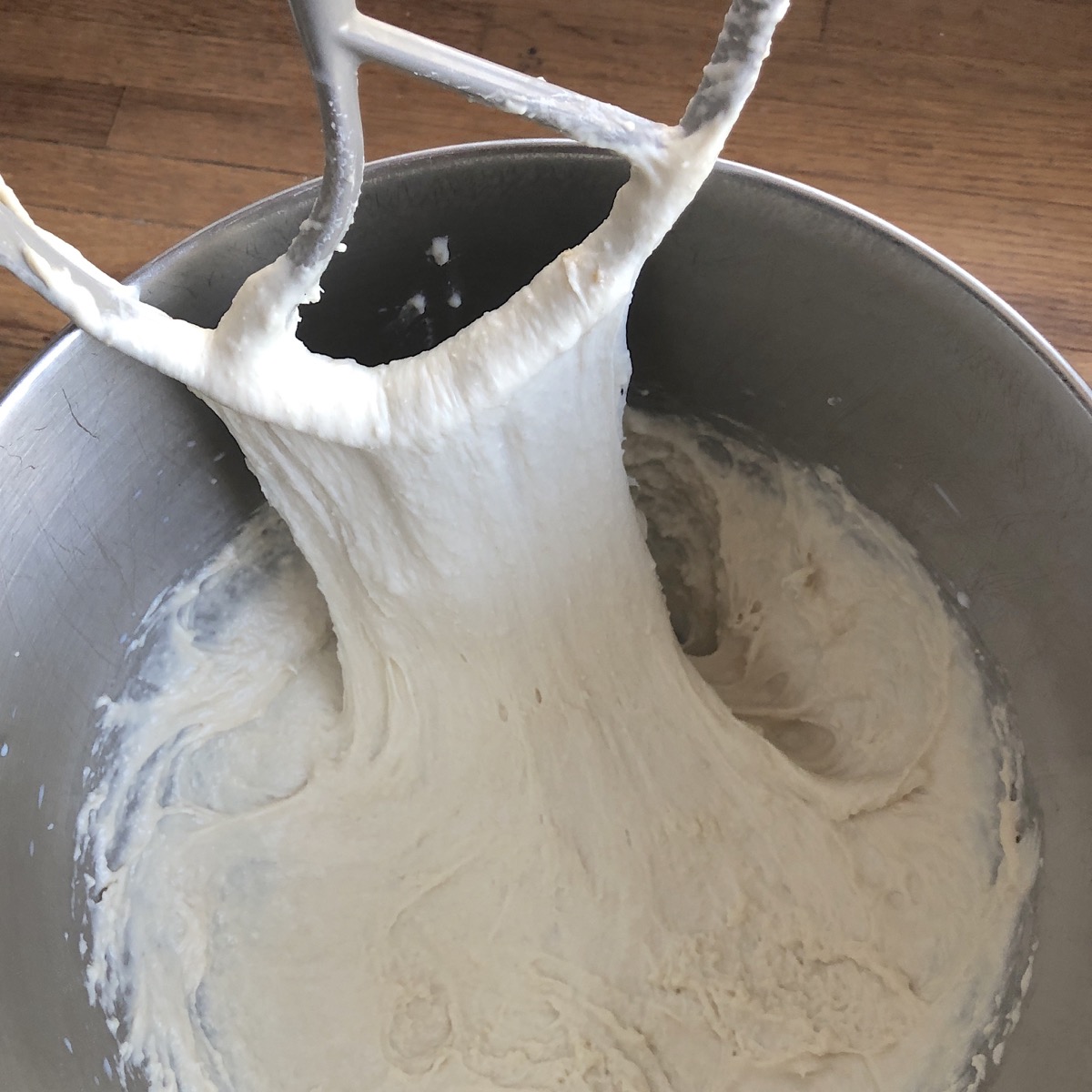 Soft yeast dough in bowl with the beater stretching some up and out, showing its gluten development.