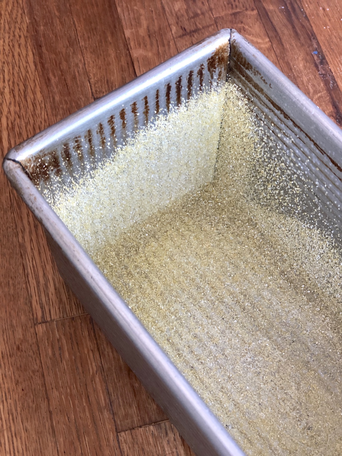 A 9" x 9" x 9" loaf pan, looking down from above to see its straight sides and a heavy dusting of cornmeal in its interior.