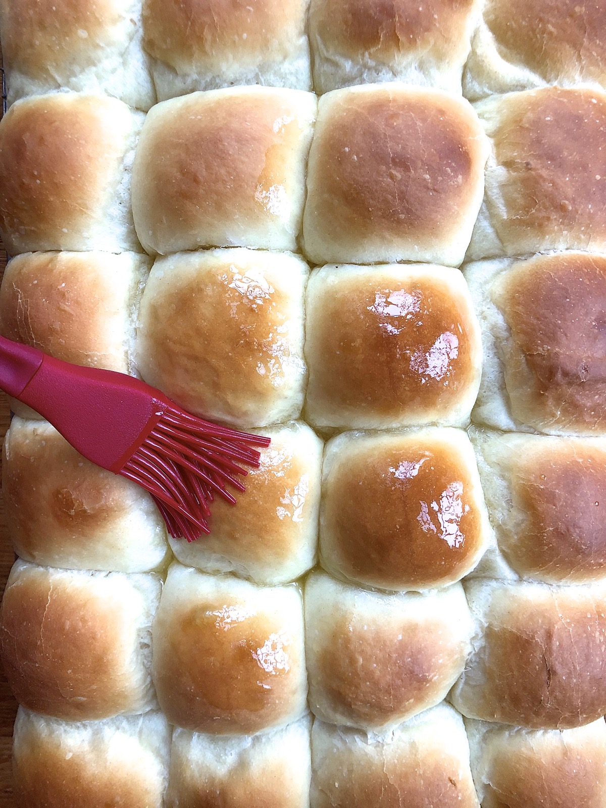Amish Dinner Rolls hot from the oven, being brushed with butter.