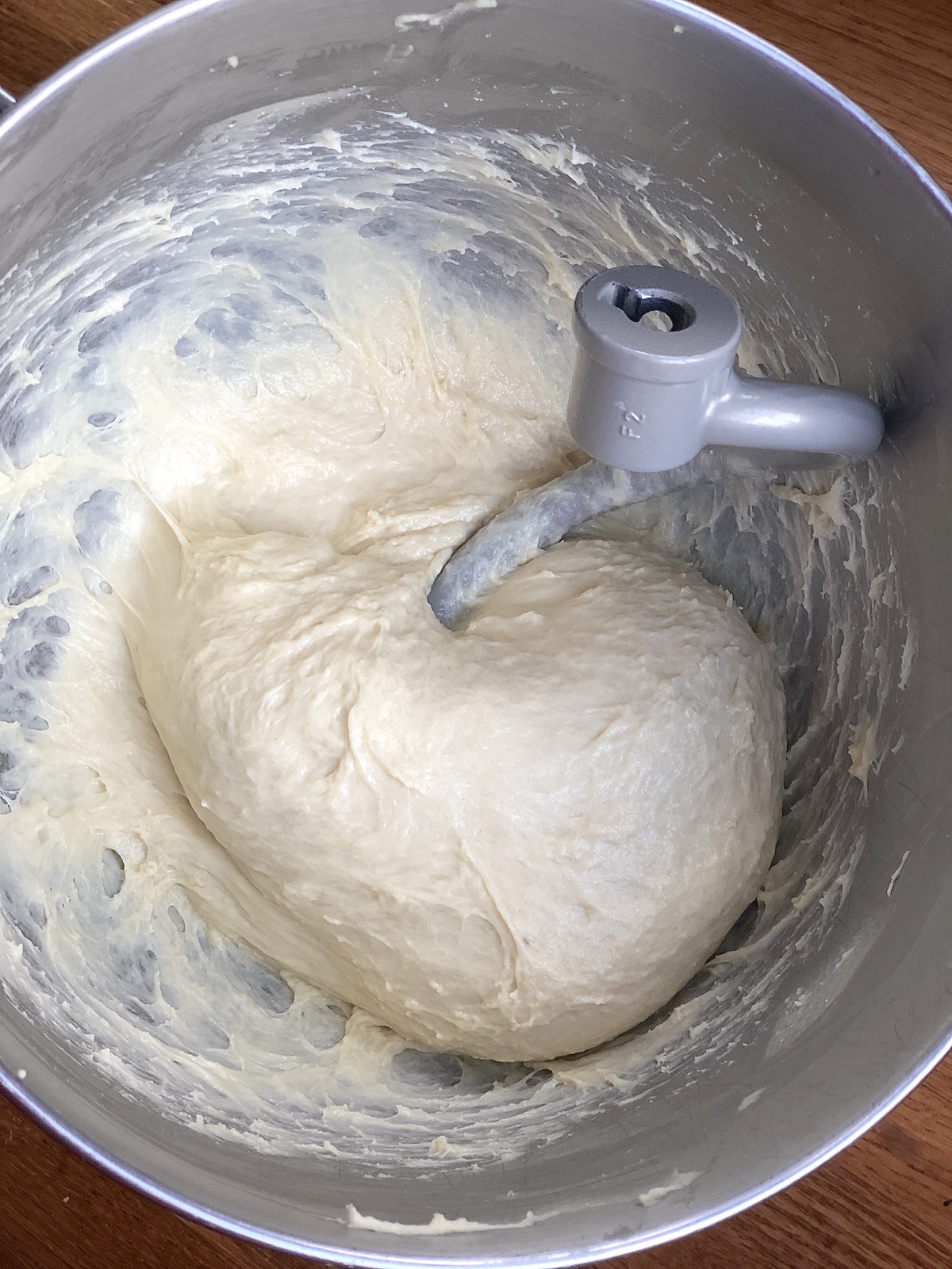 Dough for Amish Dinner Rolls in the bowl of a stand mixer, kneaded but still very sticky and clinging to the sides and bottom of the bowl.