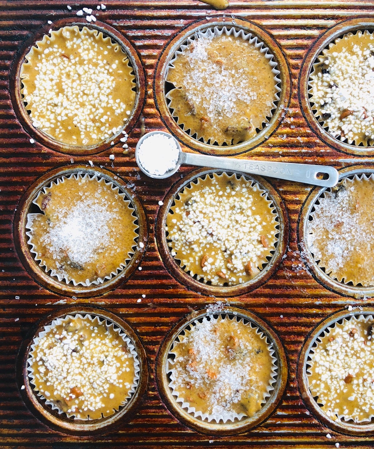 Muffin batter in a pan, some sprinkled with coarse white sugar, some with bright white Swedish sugar.