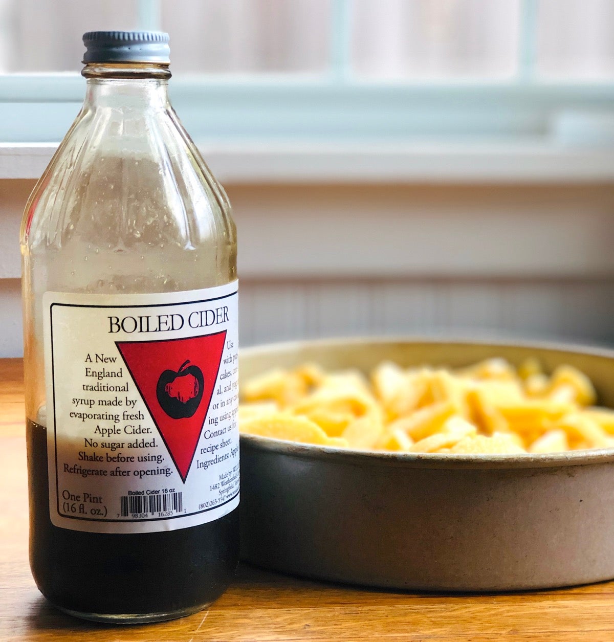 Bottle of boiled cider net to a round baking pan of chopped apples.