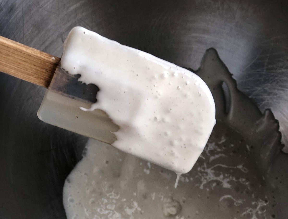 Sourdough starter dripping from a rubber spatula into a bowl.